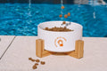 White ceramic pet bowl with a wooden stand.
