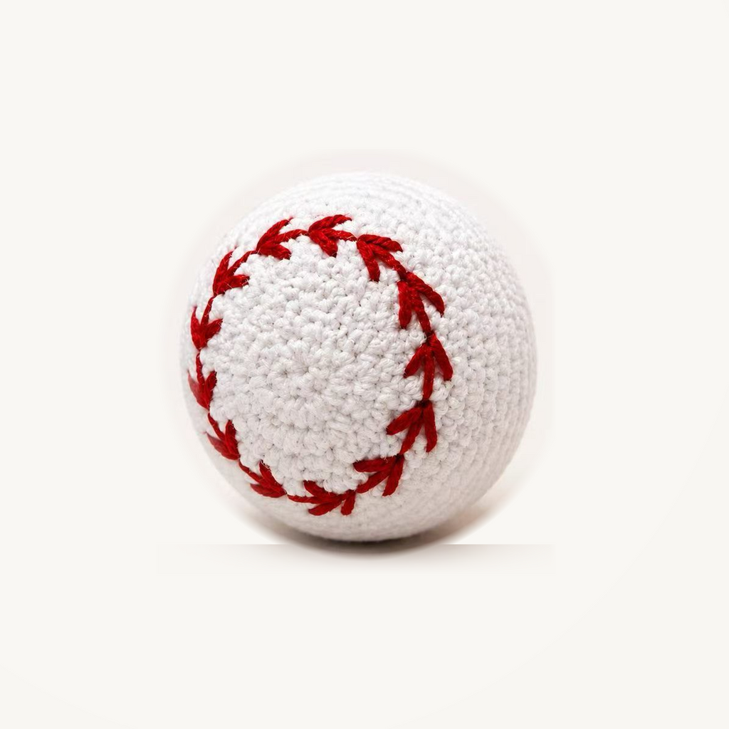 White crochet-style baseball dog toy with red stitching, on an ivory background; approximately 8 cm.